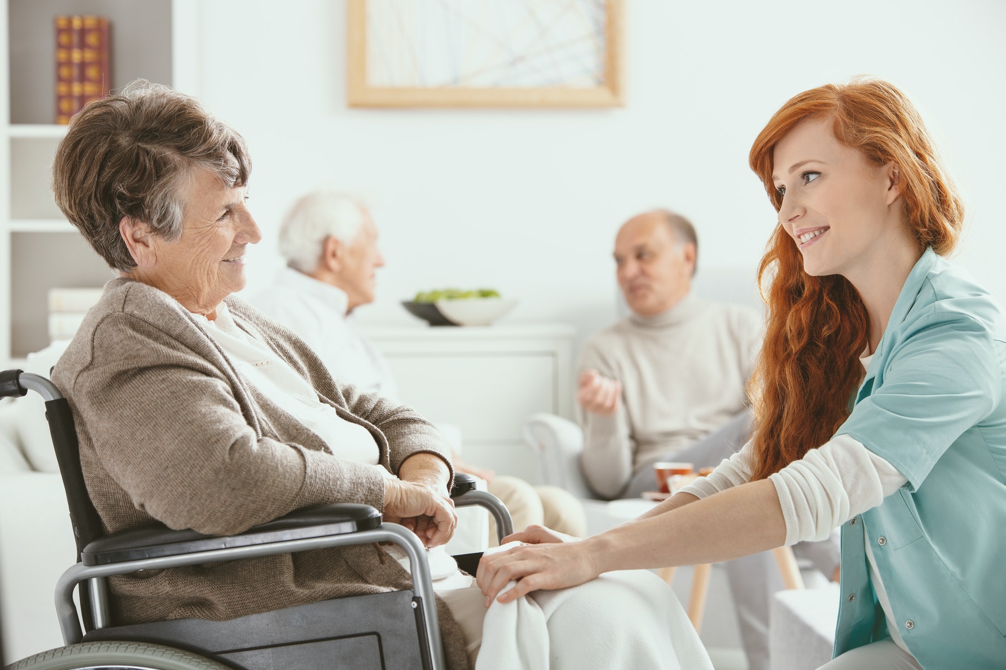Redhead smiling nurse helping senior patient in hospice